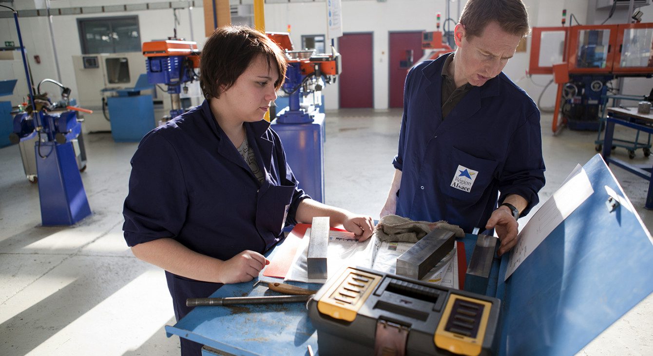Deux apprentis travaillant sur une machine dans un atelier pour acquérir une expérience pratique dans leur domaine d'études.